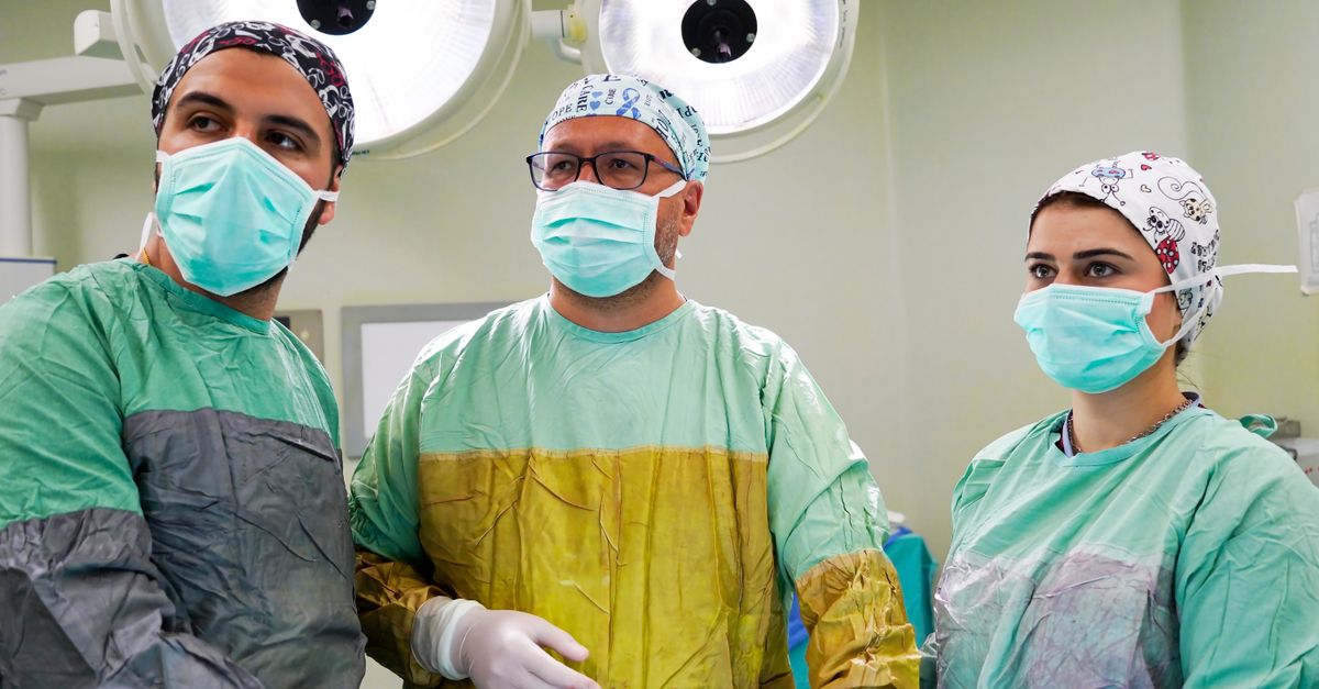 Medical team of surgeons in an operating room, wearing masks and gowns, focused on surgical procedures.