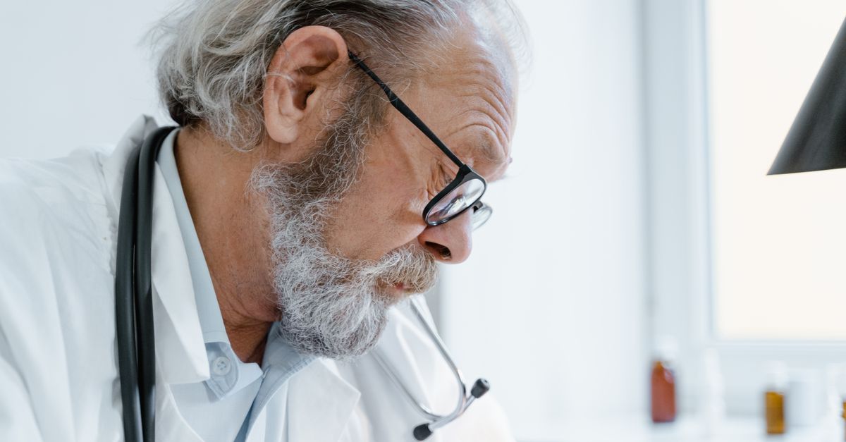 Senior doctor with glasses and stethoscope focused on work in a medical office.