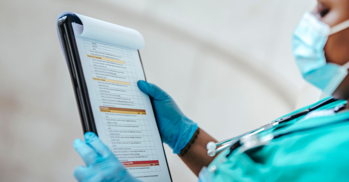 Side view of crop African American female medic in uniform reading text on paper at work