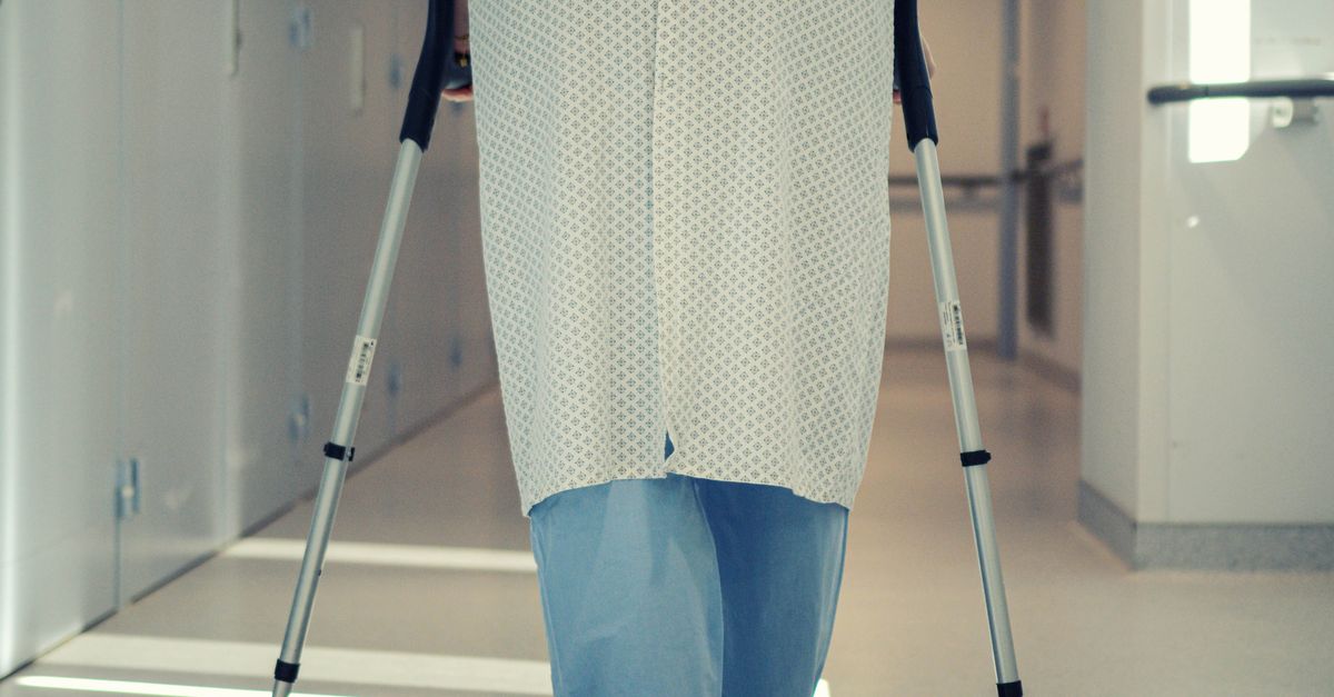 A senior patient using crutches to walk down a hospital corridor, symbolizing recovery and mobility assistance.