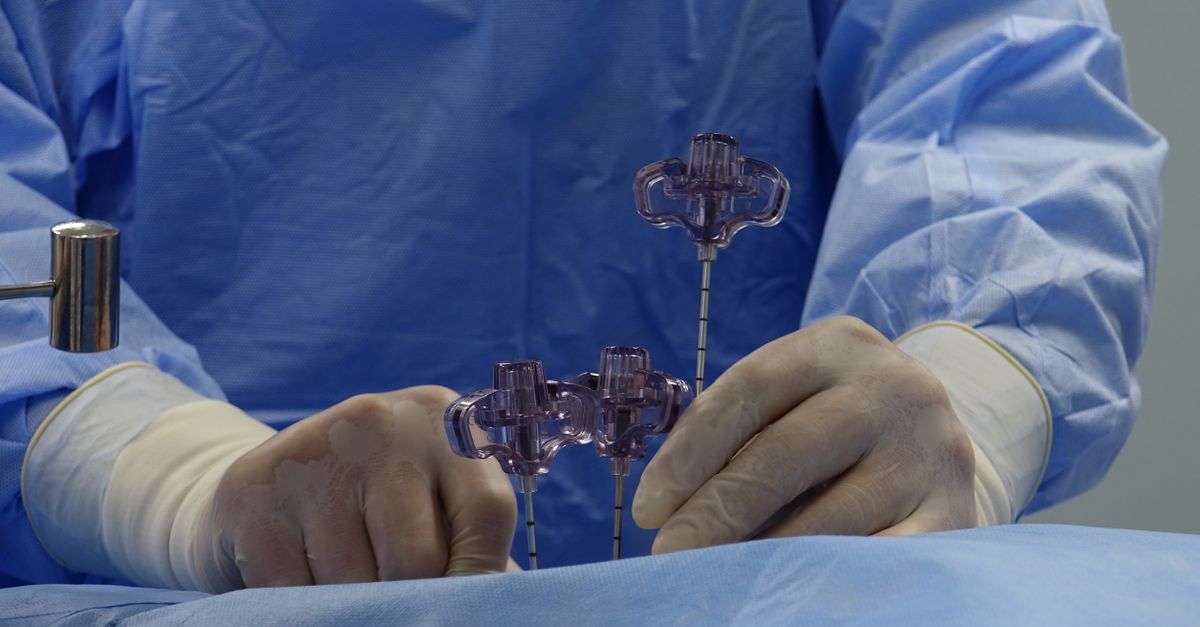 Close-up of a surgeon's hands wearing gloves and operating tools in a sterile environment.