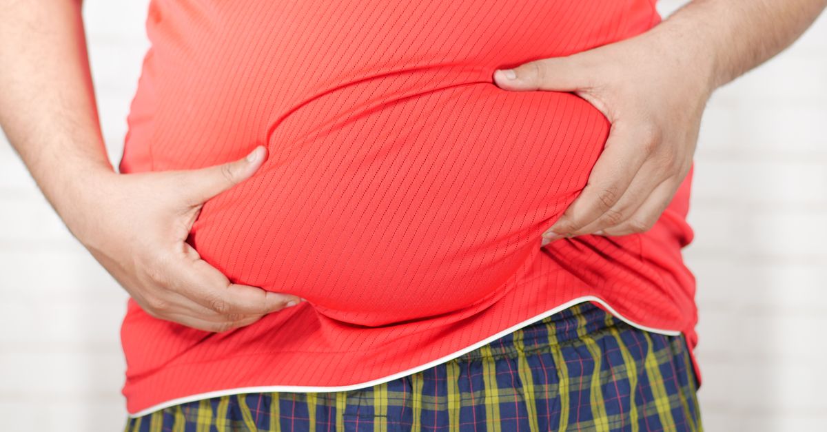 Close-up image of a man holding his bloated belly while wearing a red shirt.