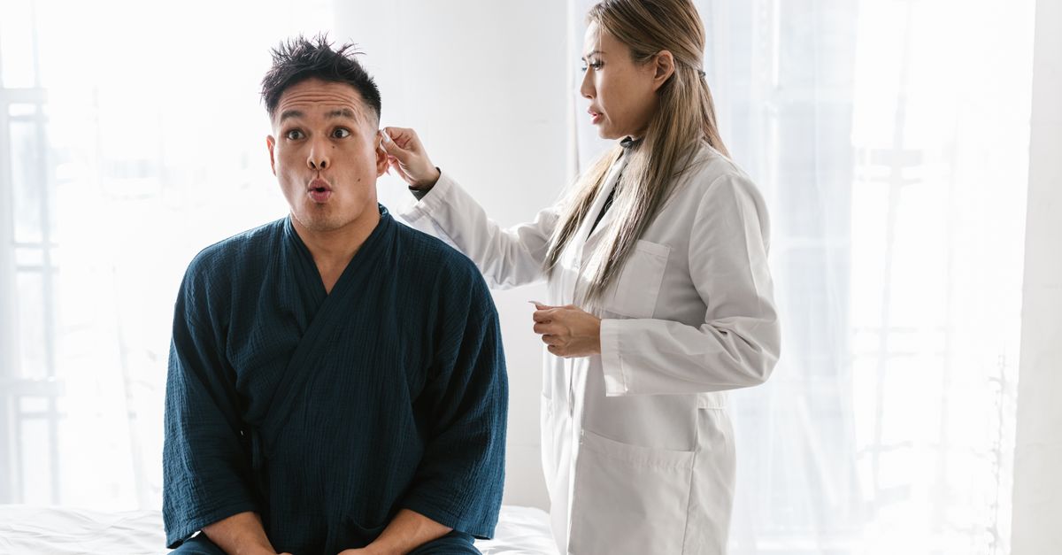 A doctor in a white coat conducts an ear exam on a patient indoors.