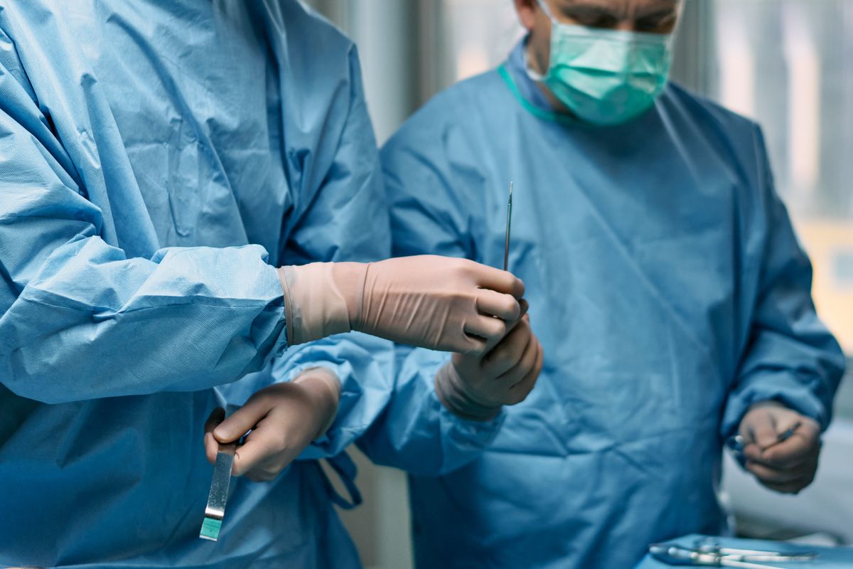 Surgeons in blue gowns handling instruments in an operating room.