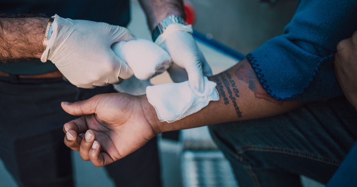 A healthcare professional in gloves applying a bandage to an injured arm, focusing on first aid care.